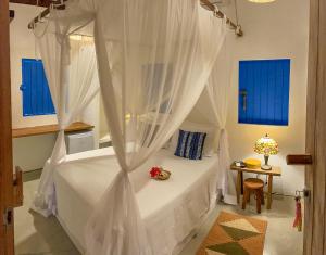 um quarto com uma cama de dossel branca e janelas azuis em Nossa Casa Caraíva - A melhor localização da Vila em Caraíva