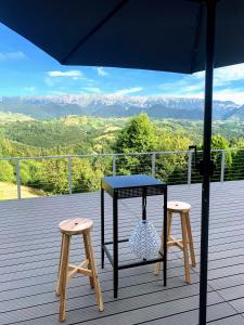 a table and two stools on a deck with mountains at Casa Stelar - A breathtaking view in Moieciu de Jos