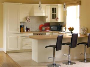 a kitchen with white cabinets and black bar stools at Dolmen Cottage in Kilfenora
