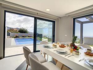 a dining room with a table and chairs and a pool at Villa de la Ponte by Atlantic Holiday in Arco da Calheta