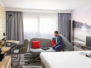 
a man sitting on a couch in a living room at Novotel Birmingham Airport in Bickenhill
