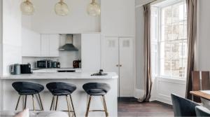 a kitchen with white cabinets and black stools at The Portland Apartment - Georgian Building with parking in Bath