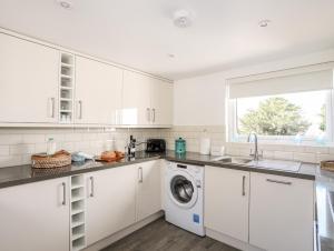 a kitchen with white cabinets and a washing machine at Crud Y Mor in Llanfairfechan