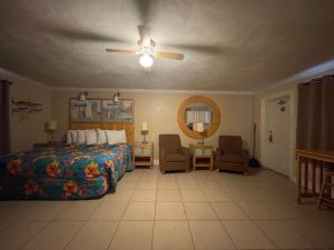 een slaapkamer met een bed en 2 stoelen en een plafondventilator bij Sea Vista Motel in New Smyrna Beach