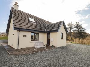 een klein wit huis met een bankje ervoor bij Sealladh an Locha Cottage in Kensaleyre