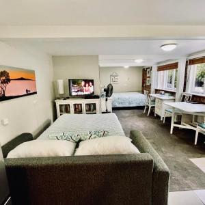 um quarto com uma cama, um sofá e uma televisão em Whitby Studio - Mairangi Bay Beach em Auckland