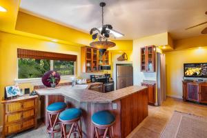 una cocina con paredes amarillas y una gran isla con taburetes azules en Kahalu'u Beach Villas 1-203 en Kailua-Kona