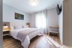 a white bedroom with a bed and a television at PENSIÓN CASA ELENA *** in Arzúa