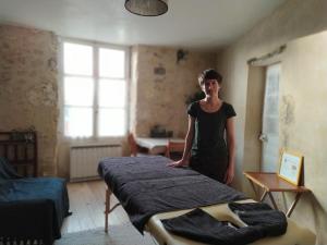 a woman standing next to a bed in a room at Au bois radieux - option massage in Bellême