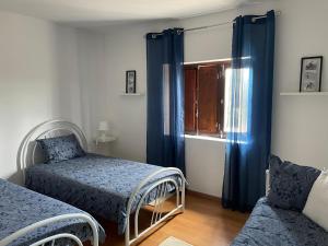 a bedroom with two beds and a window with blue curtains at Monte de Stª Margarida II in Montemor-o-Novo