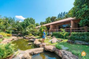 a woman standing next to a pond in front of a house at The Canal Garden Resort in Ban Huai Sua