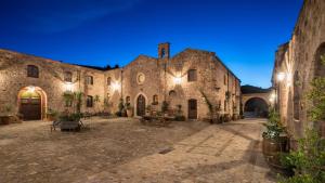 - un grand bâtiment en pierre avec une cour la nuit dans l'établissement Relais Abbazia Santa Anastasia Resort & Winery, à Castelbuono