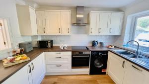 a kitchen with white cabinets and a black dishwasher at Damson Cottage - Peaceful location, charming communal orchard & private patio garden in Dittisham