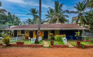 a yellow house with palm trees in the background at Vinsons Cottages in Colva