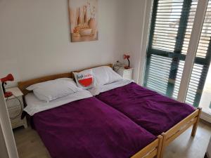a bed with purple sheets in a room with a window at 2 bedroom apartment on the coast of the Adriatic! Watermelon Marina in Marina
