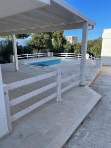 un banco de madera blanca bajo un pabellón junto a una piscina en Sine tempore beach holiday home, en Maruggio