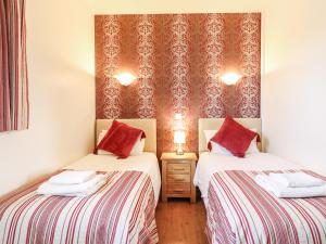 two beds in a room with red and white sheets at Barn Owl Cottage in Little Glenham