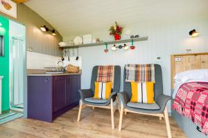 a bedroom with two chairs and a bed and a kitchen at The Big Cwtch Shepherd's Hut in Kidwelly