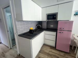 トレモリノスにあるBeach&Relax Torremolinosのピンクの冷蔵庫、白いキャビネット付きのキッチンが備わります。