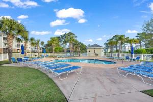 a swimming pool with blue lounge chairs and trees at Beach at the Greens in Myrtle Beach