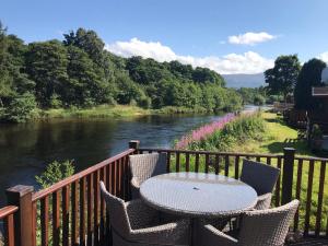a table and chairs on a balcony next to a river at Riverbank Lodge in Aviemore