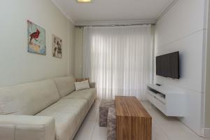 a living room with a white couch and a tv at Riomaggiore 201 -Lindo apartamento 200m da Praia de Bombas - Excelente Custo Benefício in Bombas