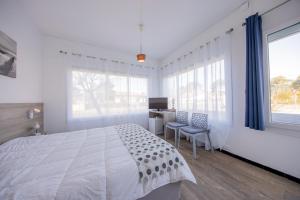 a white bedroom with a large bed and a desk at Hôtel Land'Azur in Mimizan-Plage