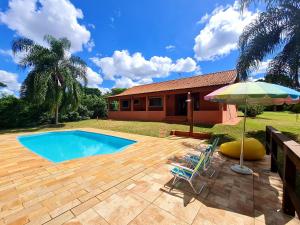 a pool with a chair and an umbrella and a house at Chácara Santo Antonio in Brotas