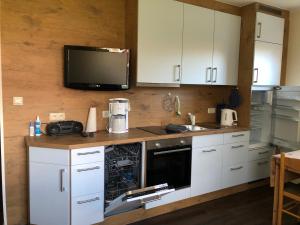a kitchen with white cabinets and a tv on the wall at Wohnung 1 mit überdachte Terrasse zum Garten Nähe Strand und Hafen Bensersiel in Bensersiel