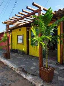 une maison jaune avec une pergola en bois et deux plantes dans l'établissement Villas de Tibau, à Pipa