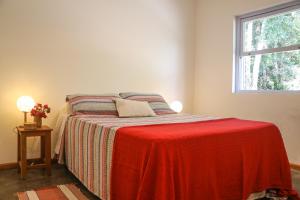 Un dormitorio con una cama con una manta roja y una ventana. en REFÚGIO FAMILIA, descanso e conexão c natureza, en Ibiúna
