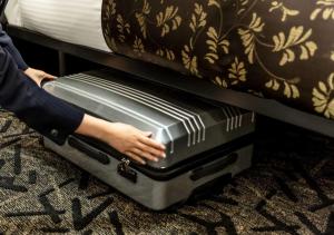 a person is holding a suitcase under a bed at APA Hotel Hakata Higashihieekimae in Fukuoka