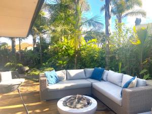 a patio with a couch and a table and palm trees at Palm Garden Beach House in Papamoa