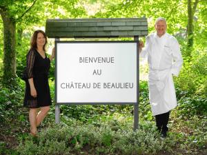 Un uomo e una donna in piedi accanto a un cartello di Le Château De Beaulieu a Busnes