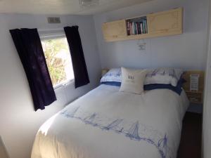 een slaapkamer met een wit bed met blauwe kussens en een raam bij Happydaze Caravan in Bacton