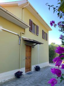 uma casa amarela com uma porta de madeira e flores roxas em casa vacanze la palma em Marina di Campo
