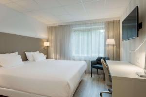 a hotel room with a large white bed and a desk at NH Eindhoven Conference Centre Koningshof in Veldhoven