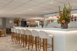 a bar with a row of white stools at NH Amsterdam Schiphol Airport in Hoofddorp