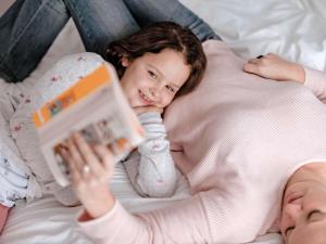 una niñita acostada en la cama leyendo un libro con su madre en ibis Kassel Melsungen, en Melsungen