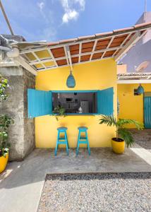 a patio with two blue stools in front of a yellow house at Pipa Magnólia Chalés in Pipa