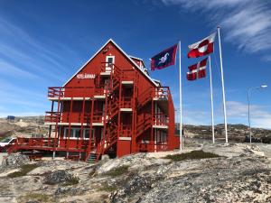 ein rotes Gebäude auf einigen Felsen mit Flaggen in der Unterkunft HOTEL SØMA Ilulissat in Ilulissat