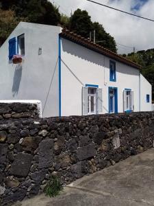 a white house with blue windows and a stone wall at Ribeira da Praia House in Vila Franca do Campo