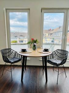 einen Tisch mit zwei Stühlen in einem Zimmer mit zwei Fenstern in der Unterkunft SUNSET APARTMENT: FREE PARKING + BALCONY + NETFLIX in Essen