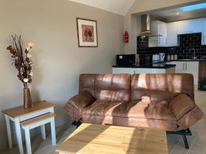 un sofá de cuero marrón en una sala de estar con mesa en Garfield Cottage en Kettering