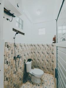 a bathroom with a toilet and a tiled wall at Dnaiko Syariah Hotel in Bukittinggi