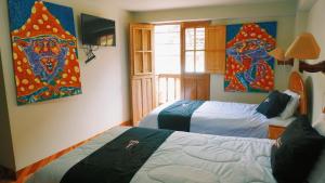 a bedroom with two beds and paintings on the wall at Colores Hotel Apu-Linli in Pisac
