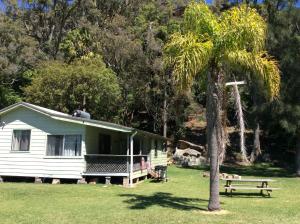 une maison blanche avec un palmier et un banc dans l'établissement Currawong Beach Cottages, à Great Mackerel Beach
