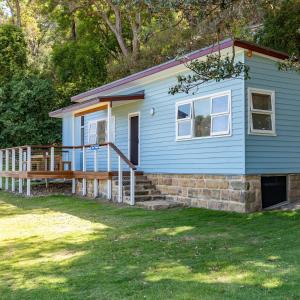 a blue house with a porch and a deck at Currawong Beach Cottages in Great Mackerel Beach
