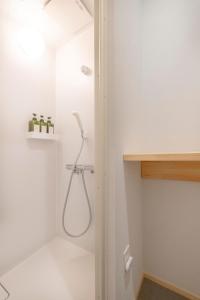 a shower in a bathroom with a white wall at Coliving & Cafe SANDO in Imabari