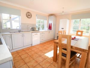 cocina con armarios blancos, mesa y sillas en Glyn Cottage, en Llanon